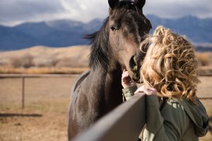 Heather Peterson of Pain Free for Good, standing with a horse with mountains in background.